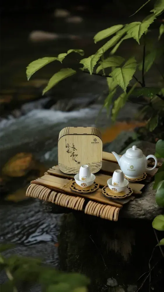 Ấm trà sứ trắng và bộ chén trà đặt bên dòng suối